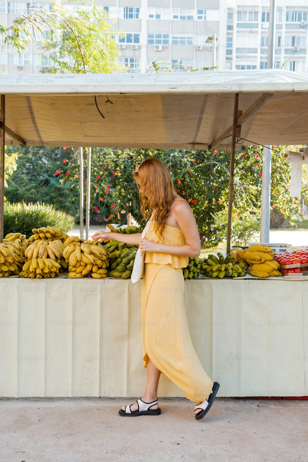 Une femme en robe jaune debout devant un stand de fruits