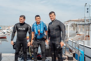 three men in wetsuits standing on a dock