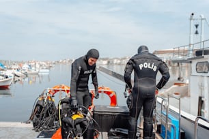 a couple of men in wet suits standing next to a boat