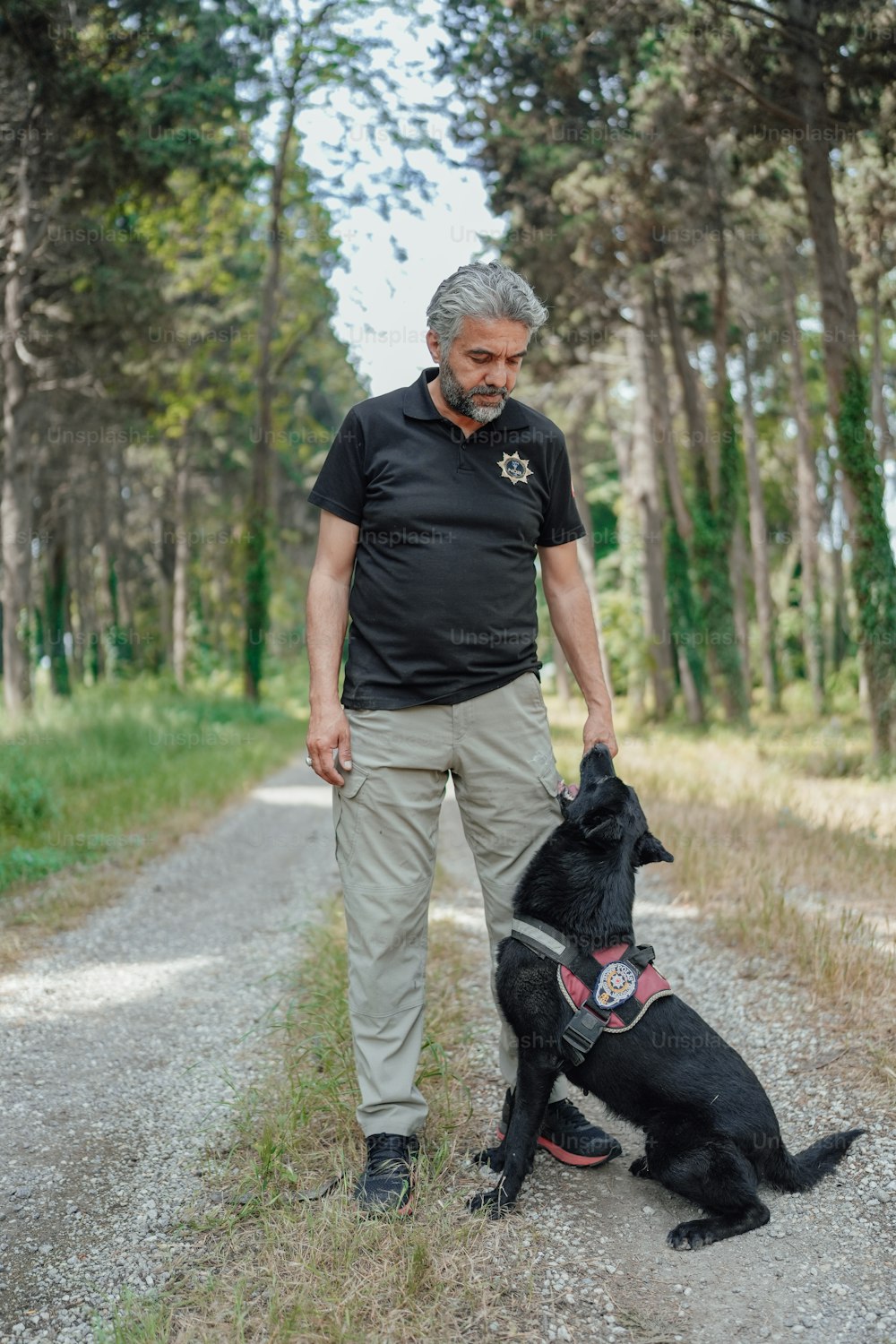 um homem ao lado de um cachorro preto em uma estrada de terra