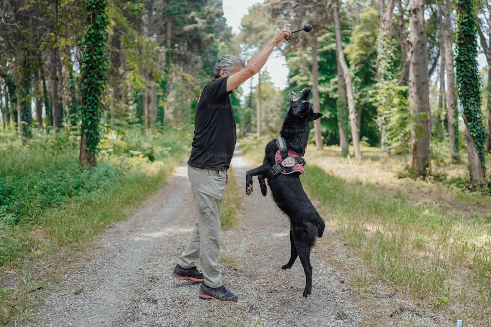 a man standing on a dirt road next to a black dog
