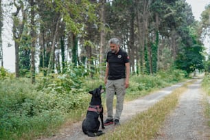 a man standing next to a black dog on a dirt road