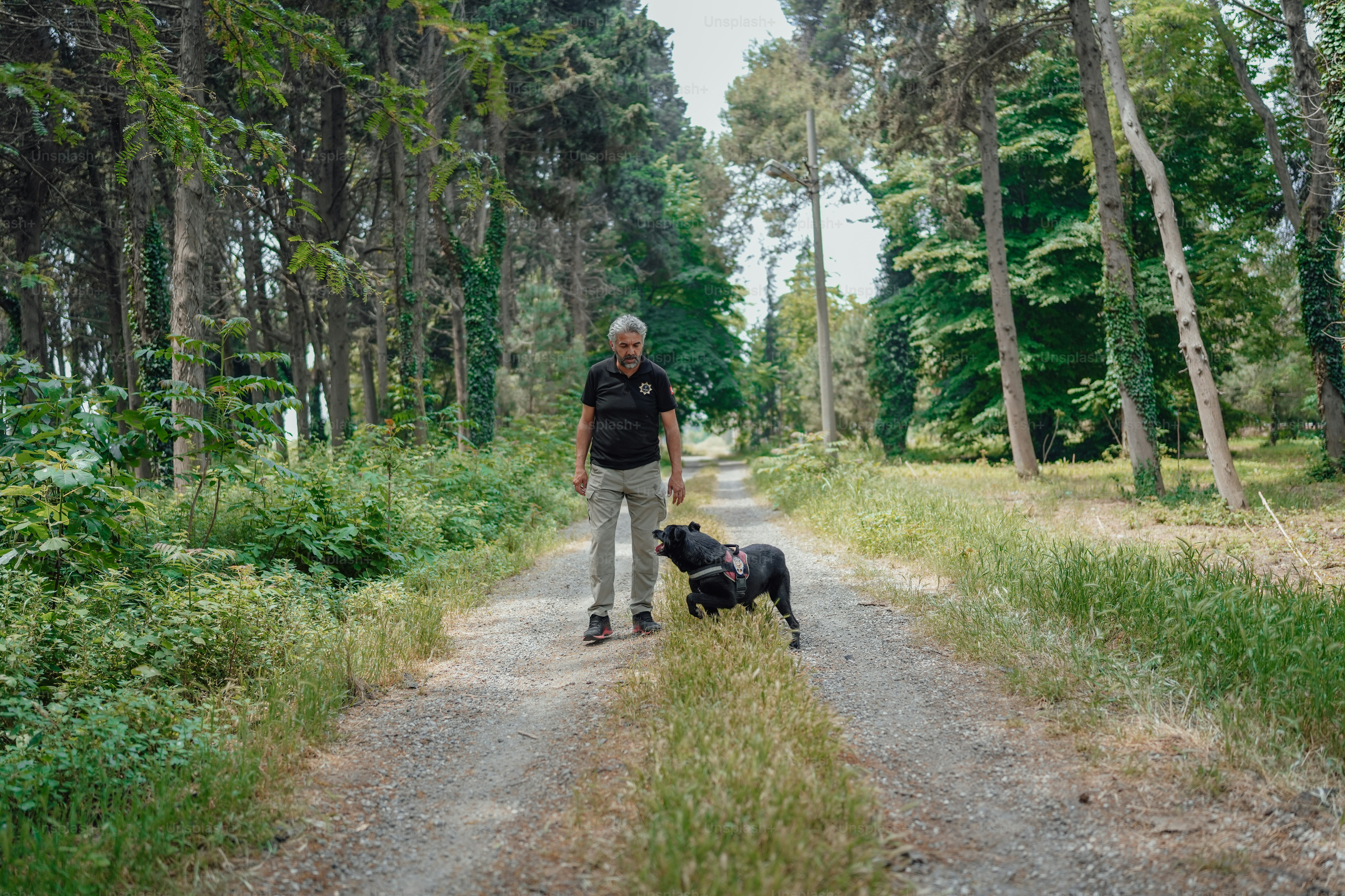 a man standing next to a black dog on a dirt road