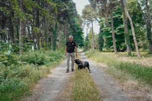 a man standing next to a black dog on a dirt road