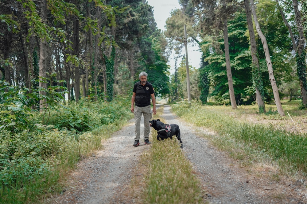 a man standing next to a black dog on a dirt road