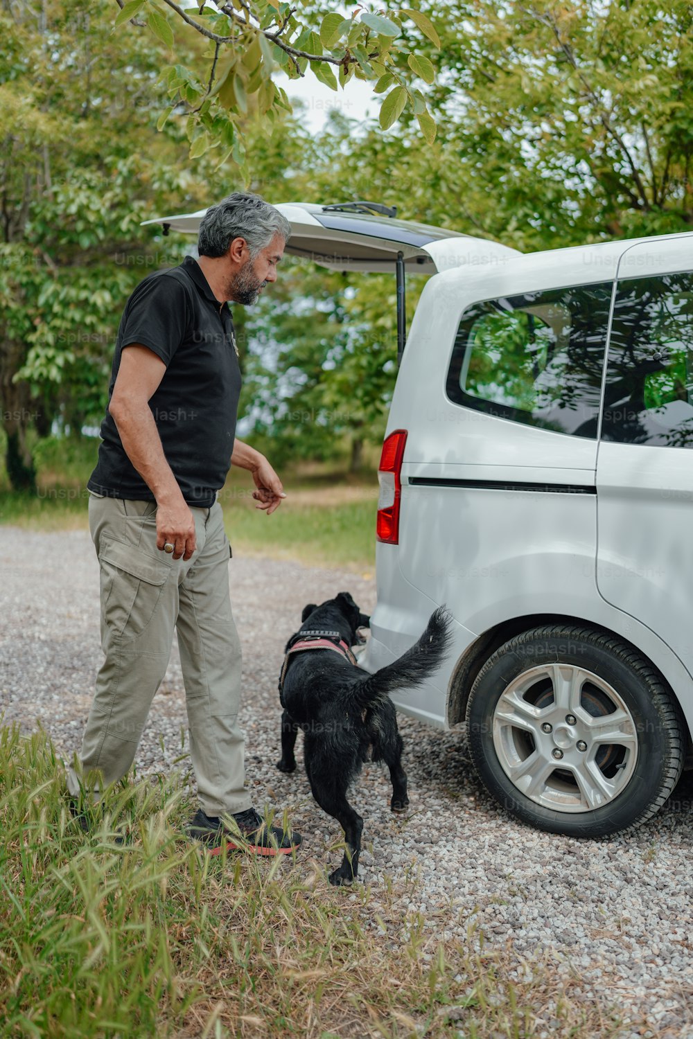 um homem ao lado de uma van branca com um cachorro preto