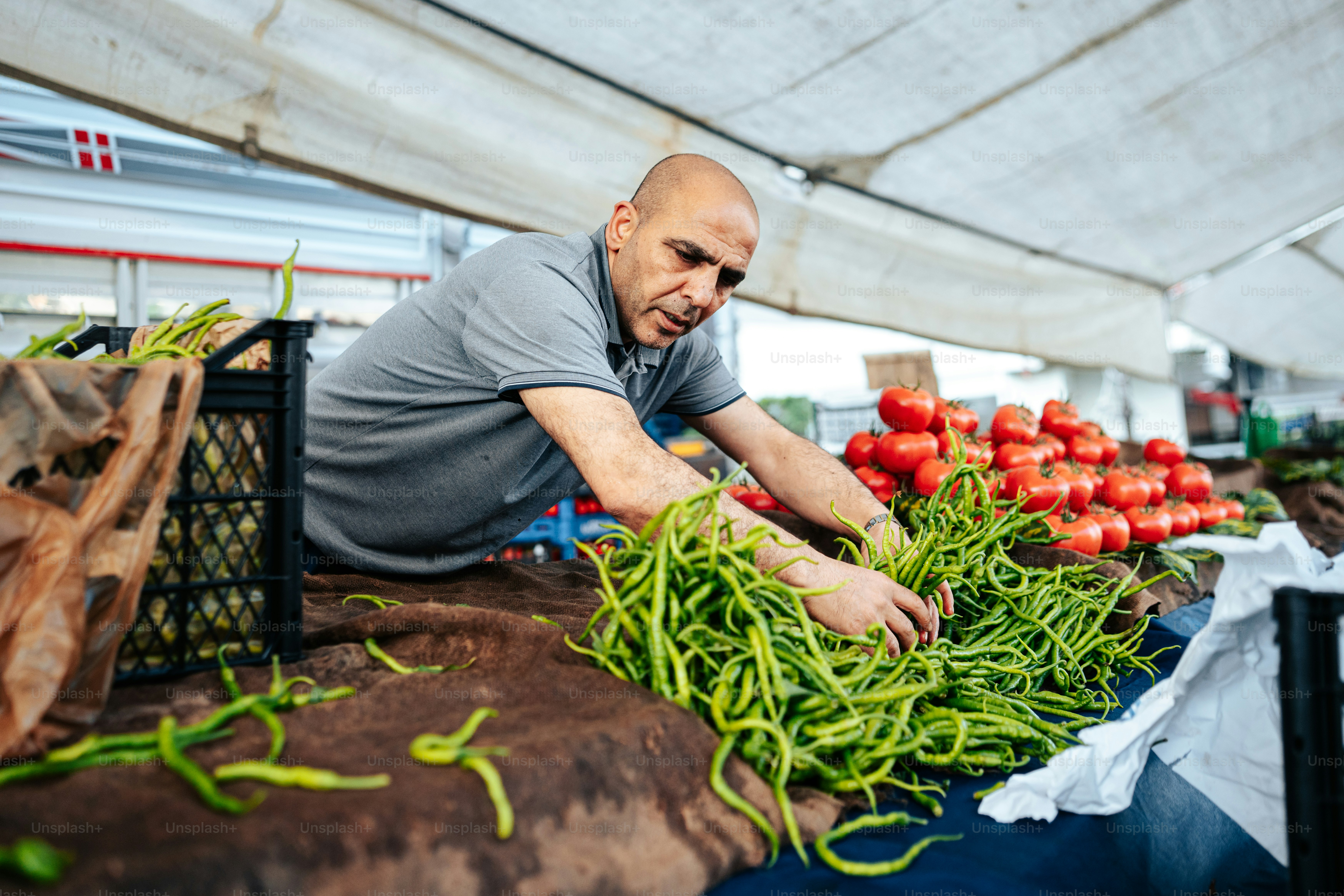 a man in grey shirt working on vegetables at a market