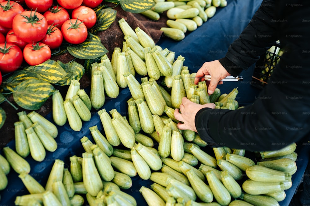 a person cutting cucumbers in front of a bunch of tomatoes
