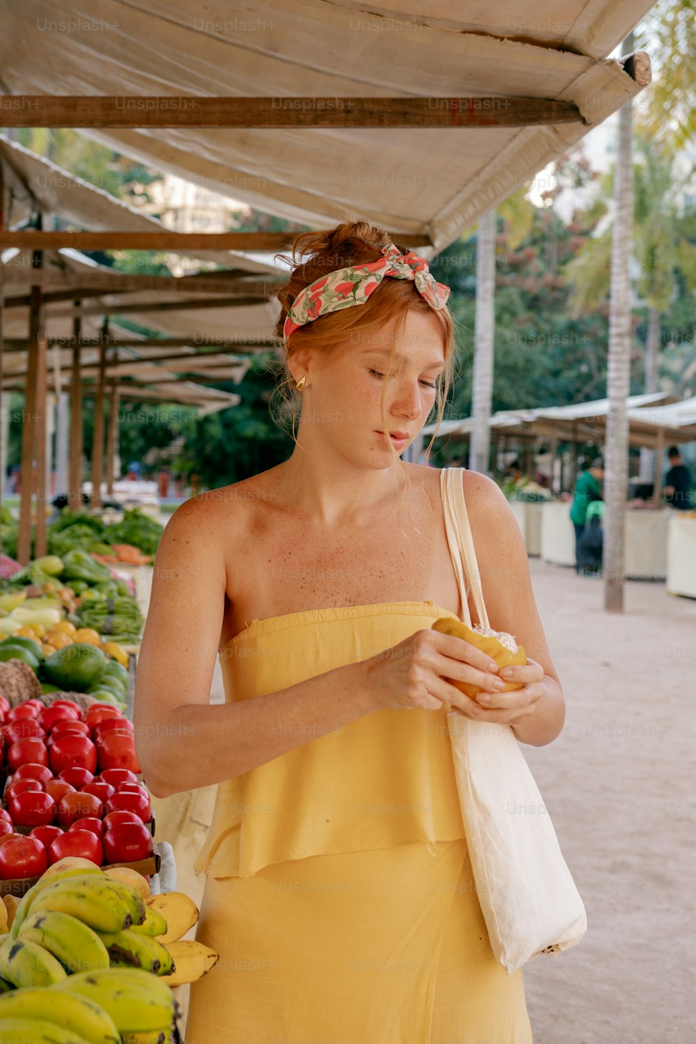 a woman in a yellow dress standing in front of a fruit stand