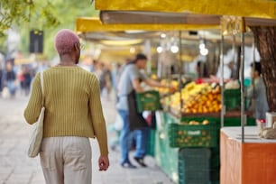 a woman walking down a street past a fruit stand