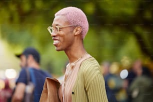 ピンクの髪と眼鏡をかけた男が微笑んでいる