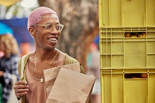 um homem com cabelo rosa e óculos segurando um saco de papel