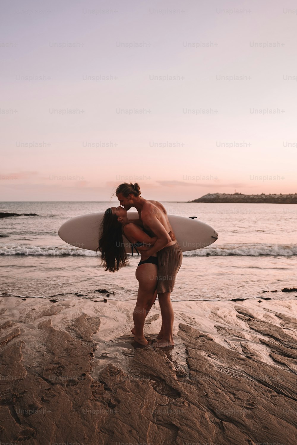 um homem e uma mulher se beijando na praia com uma prancha de surf