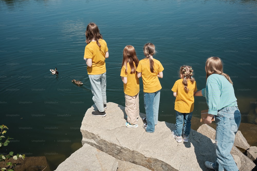 a group of young girls standing on top of a rock next to a body of