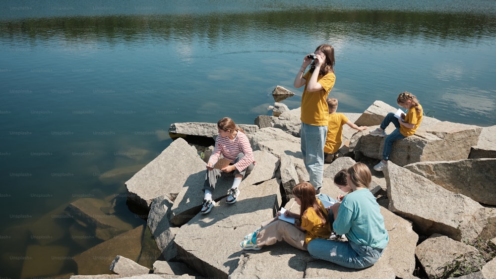 a group of people sitting on rocks next to a body of water
