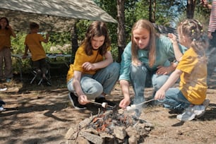 a woman and two children cooking over a campfire