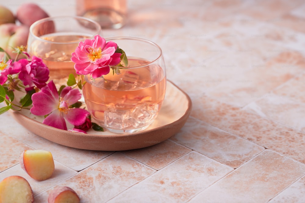 two glasses of water with pink flowers on a plate