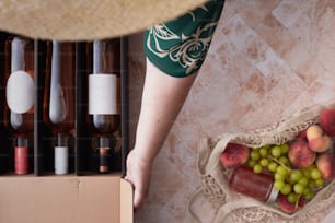 a person holding a basket of fruit next to bottles of wine