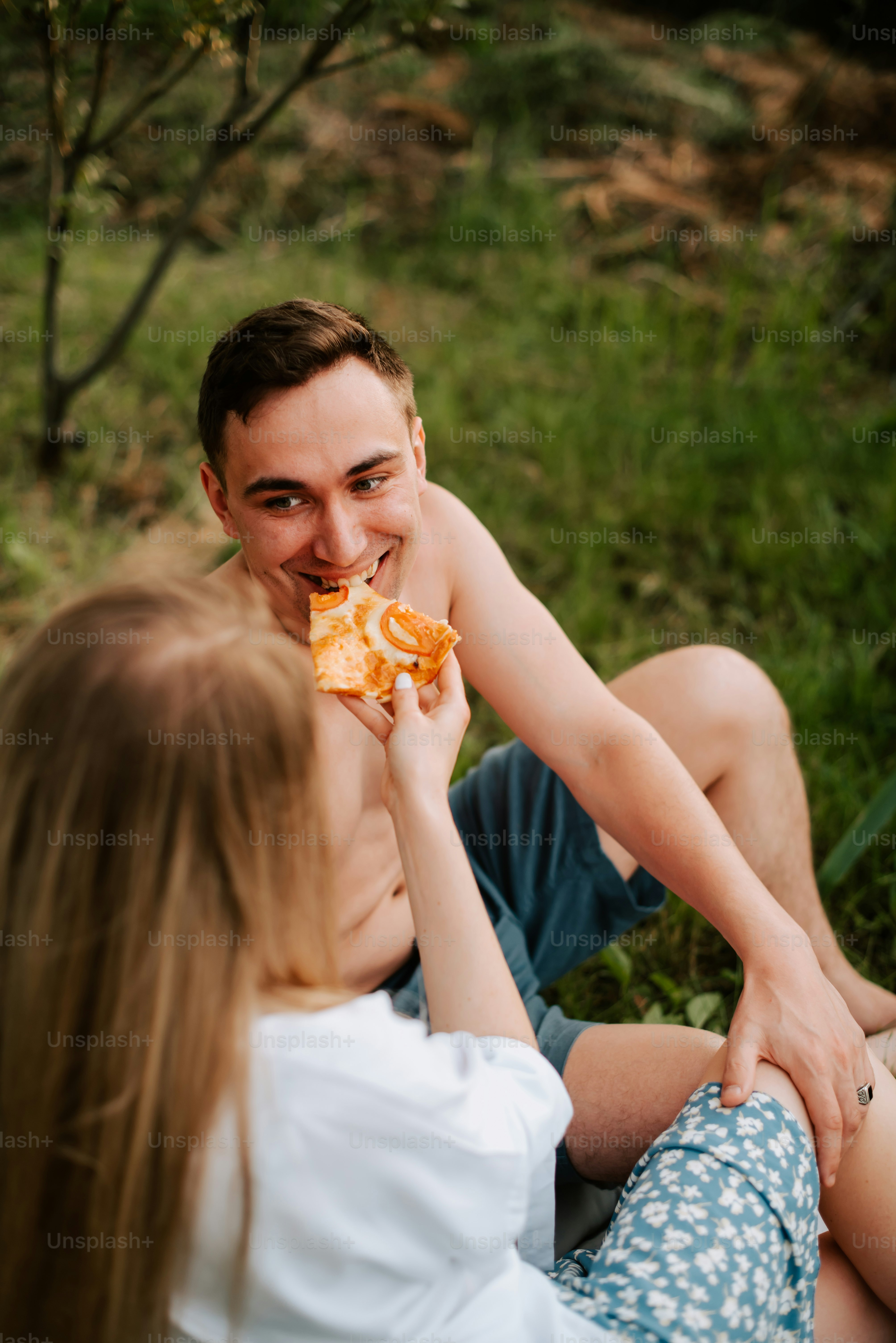 a man and a woman sitting on the ground eating pizza