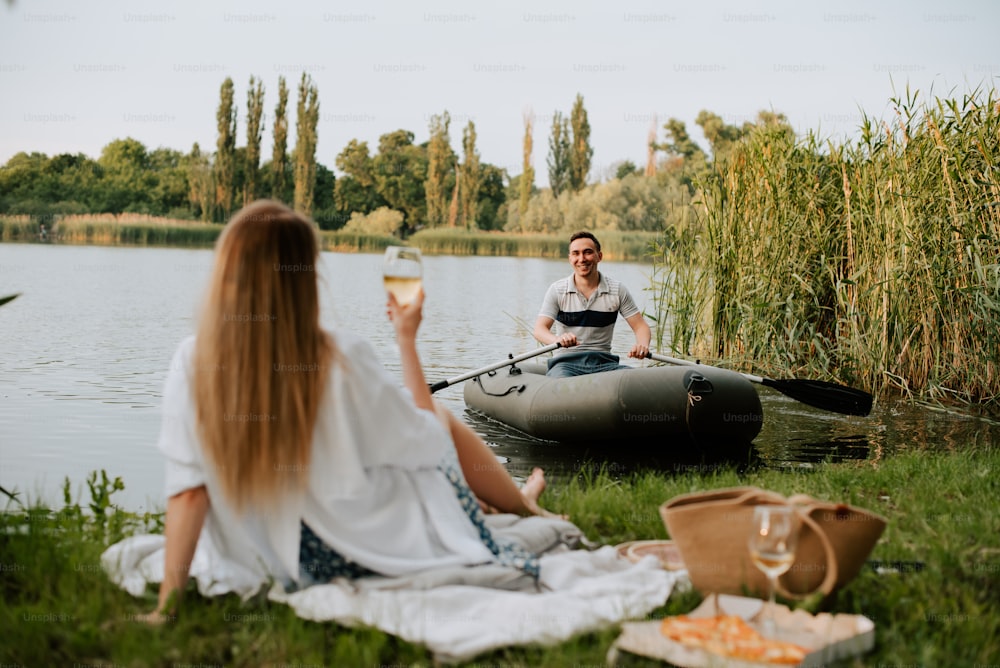 a man and a woman sitting on the grass next to a lake