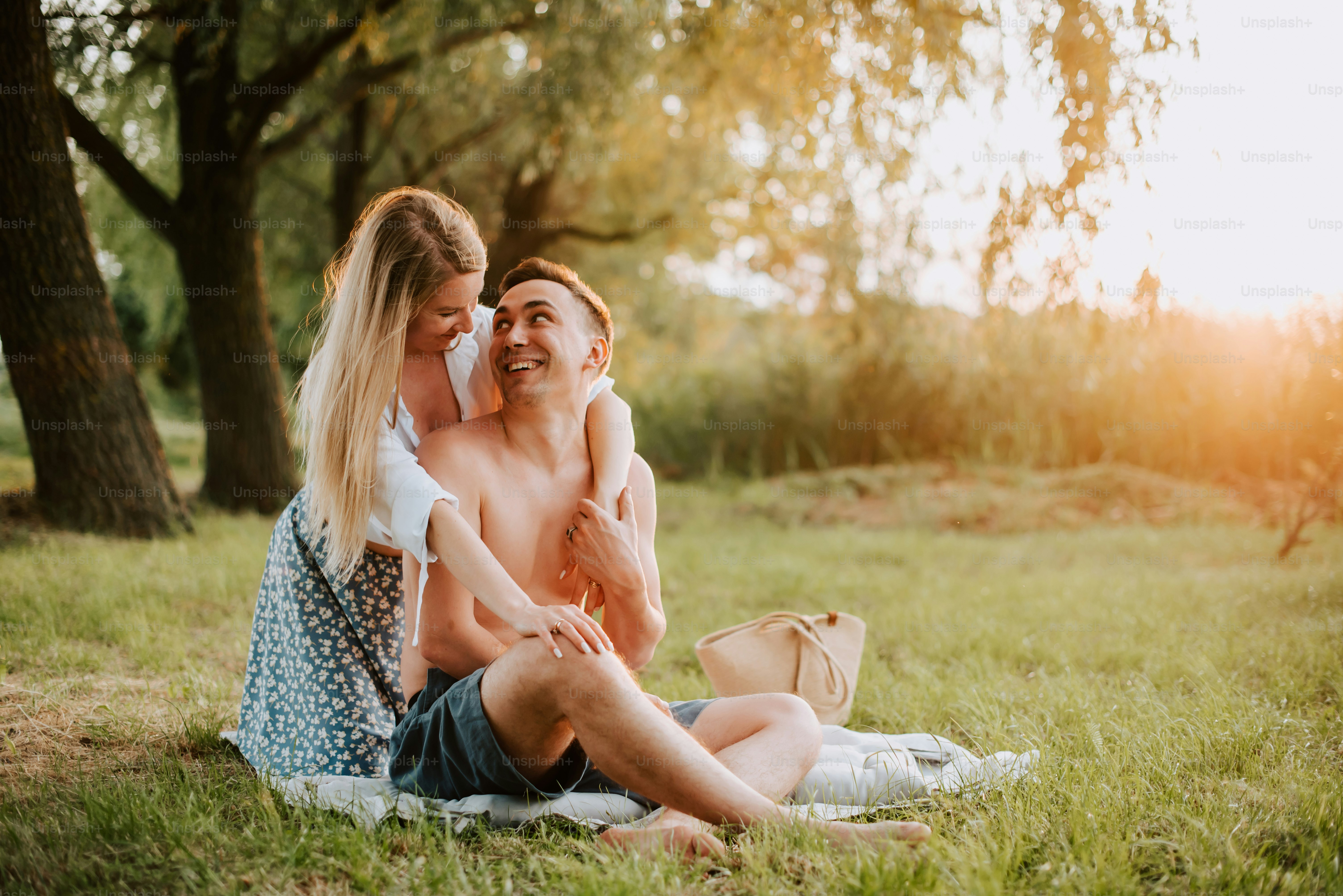 a man and woman sitting on a blanket in the grass