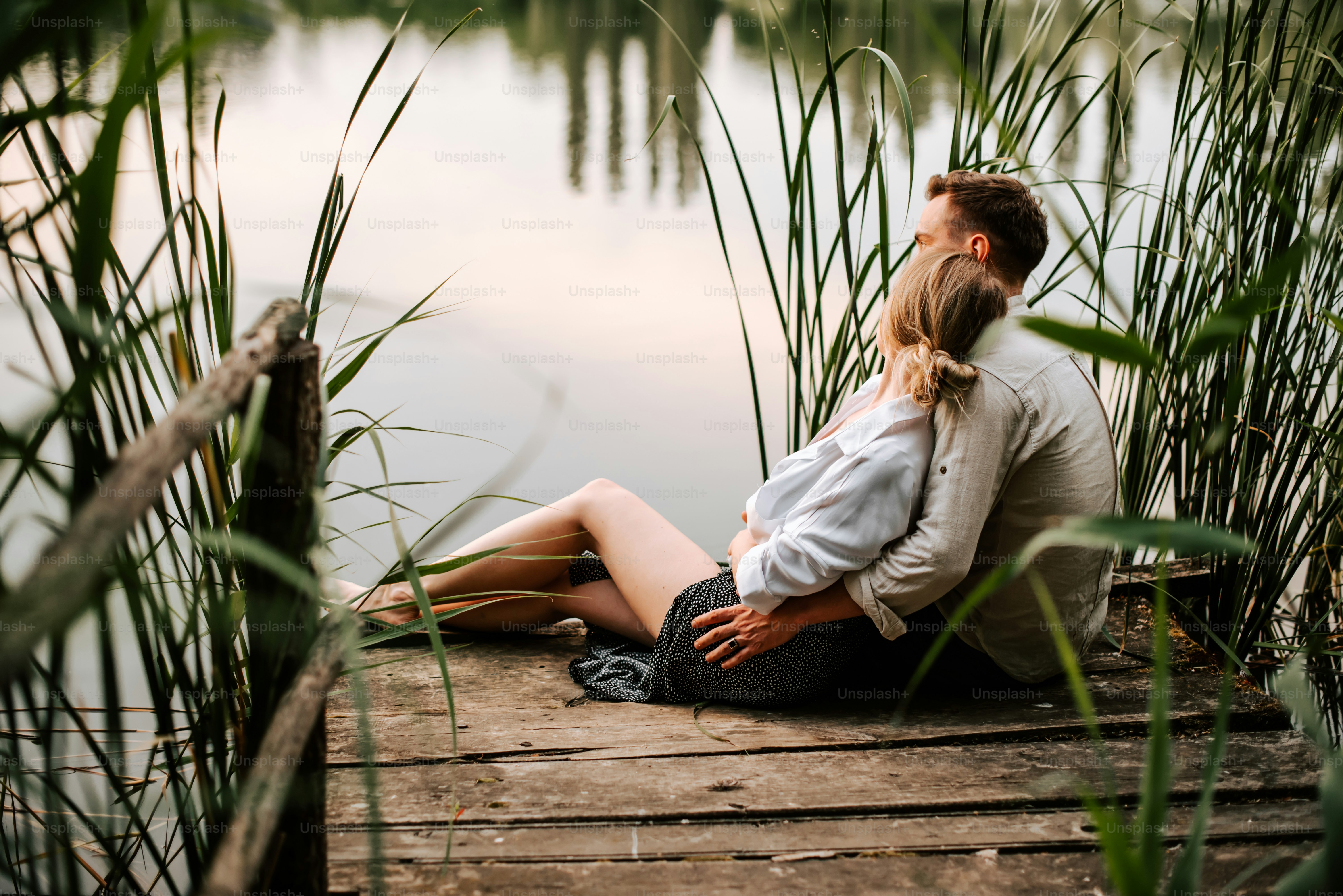 a man and a woman sitting on a dock next to a body of water