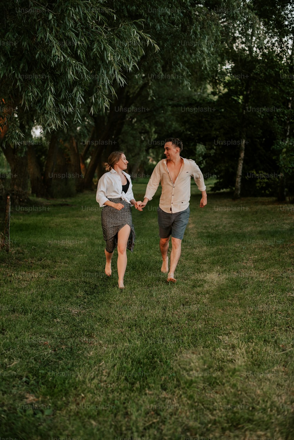 a man and woman walking through a field holding hands