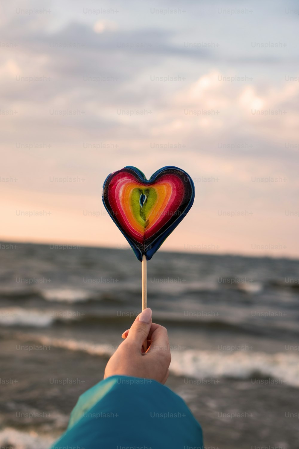 a person holding a heart shaped lollipop in front of the ocean