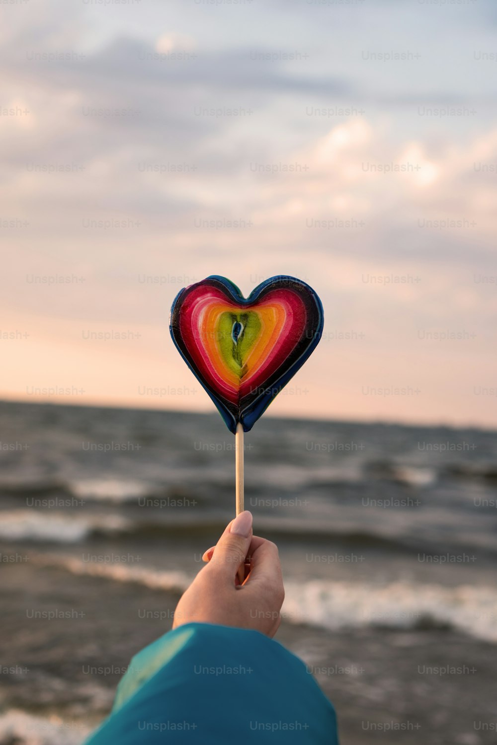 a person holding a heart shaped lollipop in front of the ocean