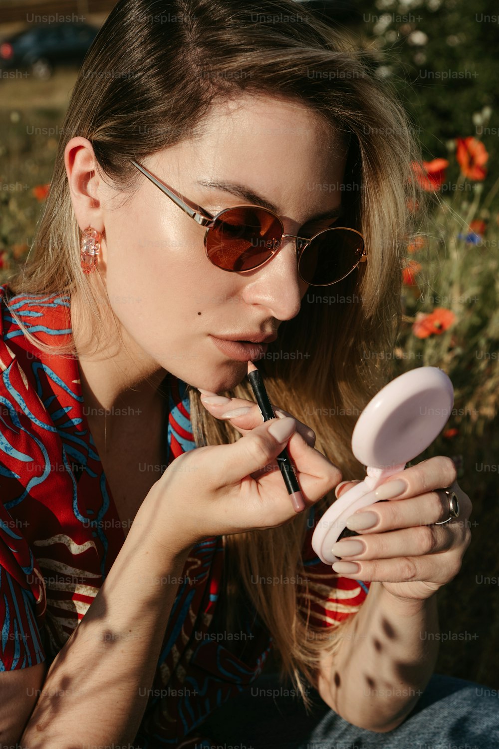 a woman in sunglasses is holding a compact mirror