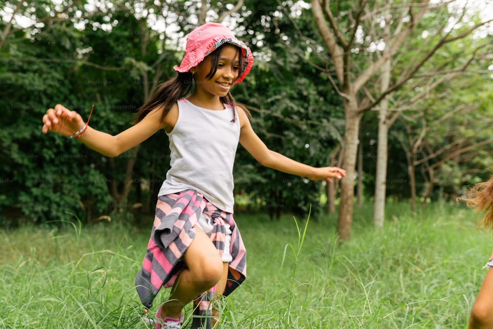 Uma menina com um chapéu rosa está correndo pela grama
