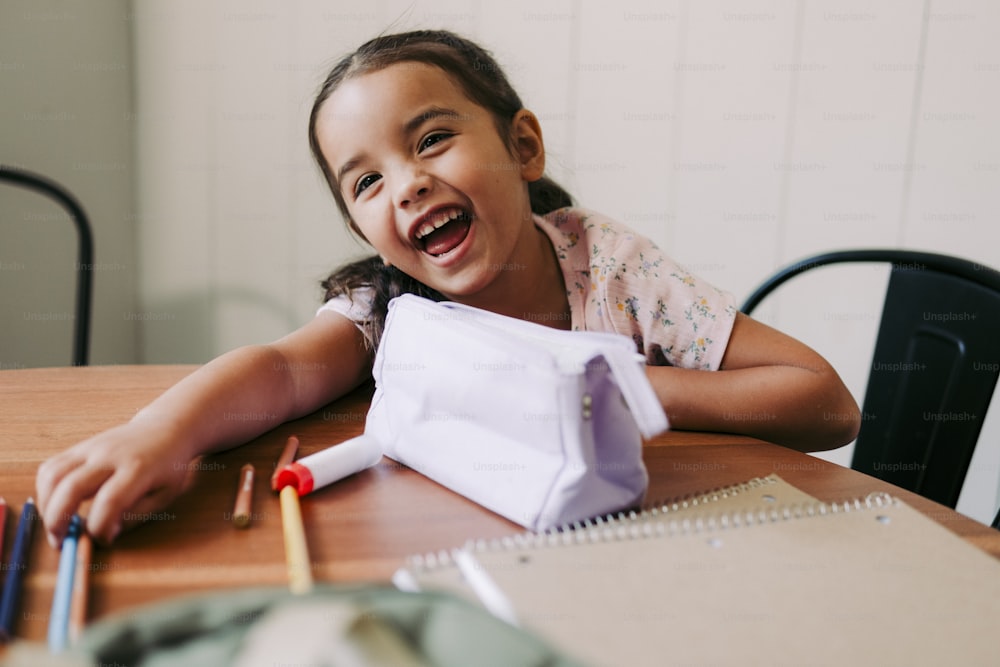 une petite fille assise à une table avec des crayons