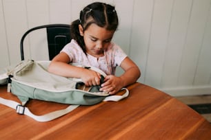 a little girl sitting at a table with a bag