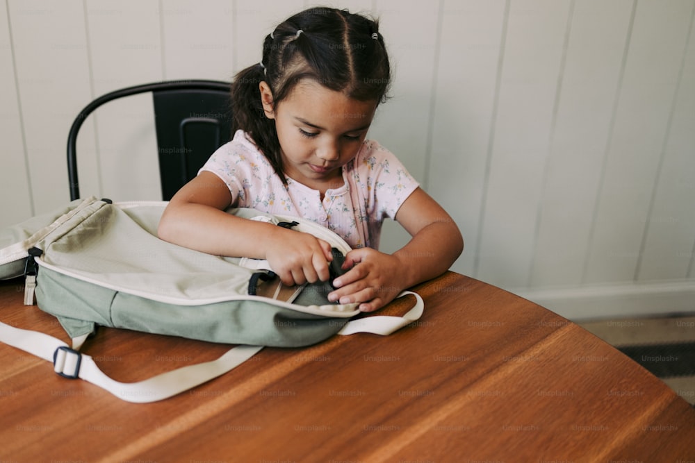 a little girl sitting at a table with a bag