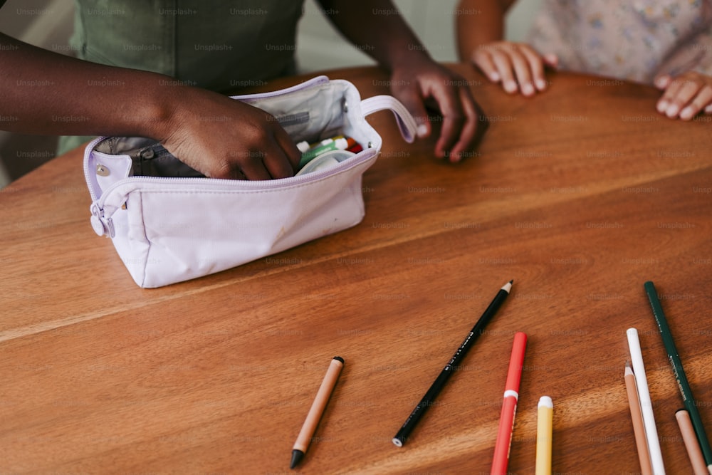 uma pessoa segurando um lápis em um saco sobre uma mesa