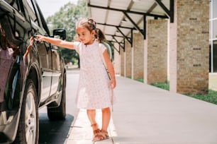 a little girl standing next to a black car