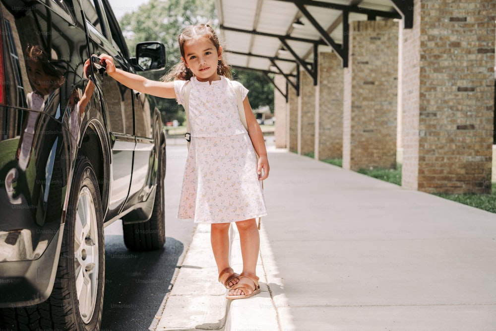 Una bambina in piedi accanto a una macchina nera