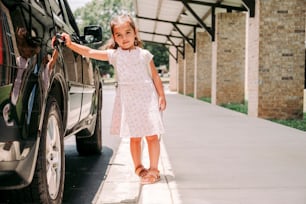 a little girl standing next to a black car