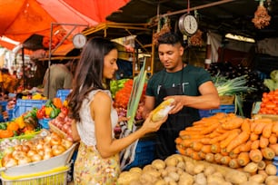 Un homme et une femme debout devant un stand de fruits et légumes