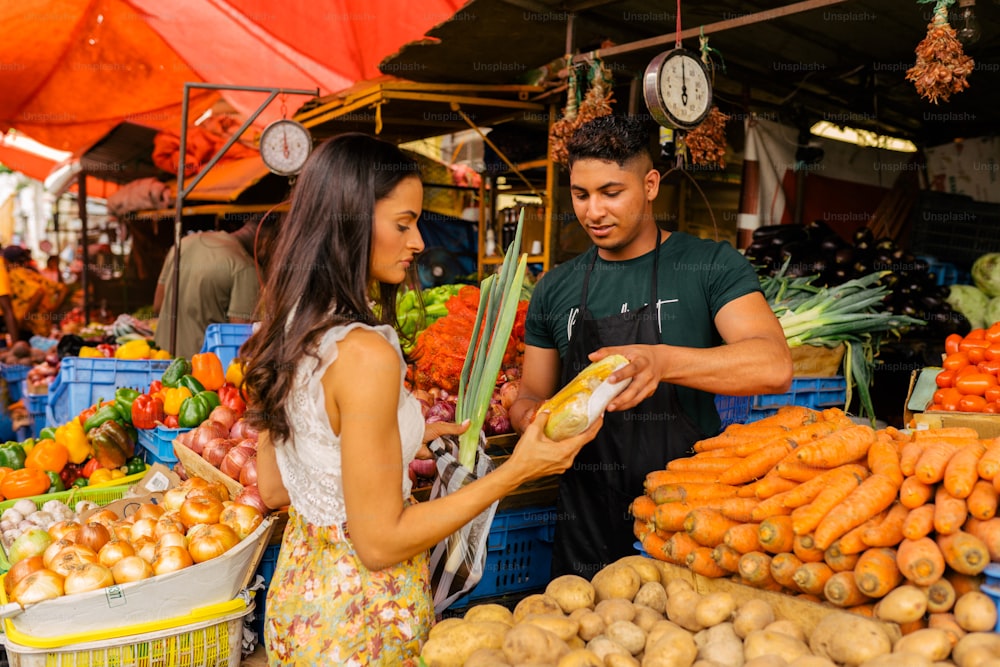Un homme et une femme debout devant un stand de fruits et légumes