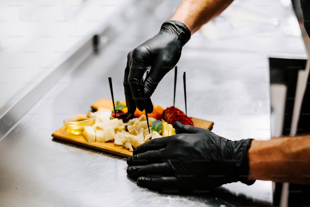 uma pessoa de luvas e luvas pretas preparando alimentos em uma tábua de corte