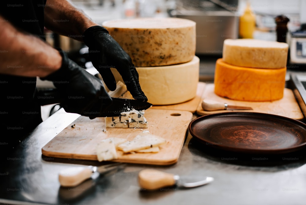 uma pessoa de luvas pretas cortando queijo em uma tábua de corte