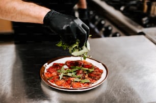 a person in a black glove is putting greens on a plate