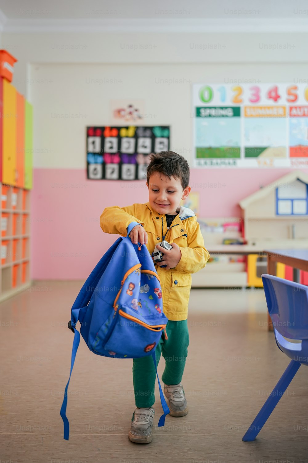 a young boy carrying a blue backpack in a classroom