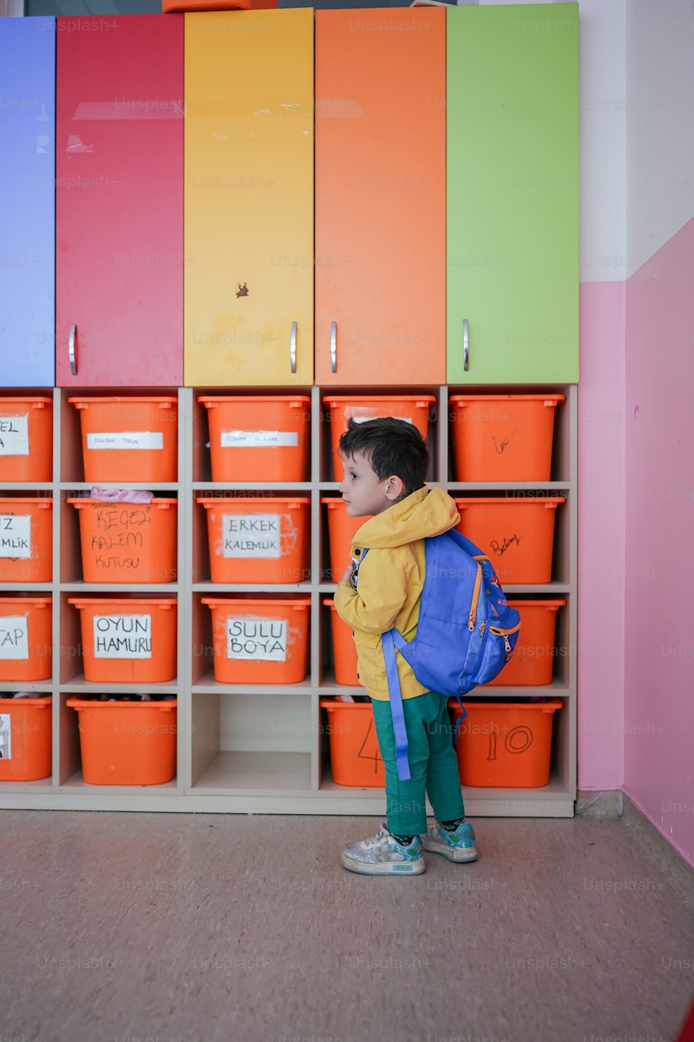 ein kleiner Junge, der vor einer Wand aus orangefarbenen und rosa Mülltonnen steht