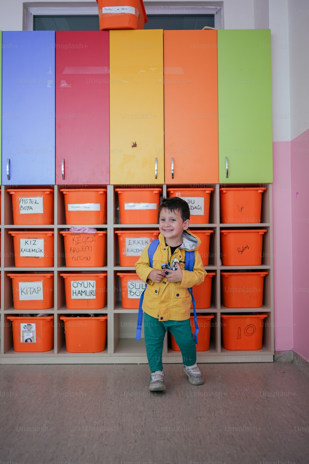 um menino em pé em frente a uma parede de lixeiras coloridas