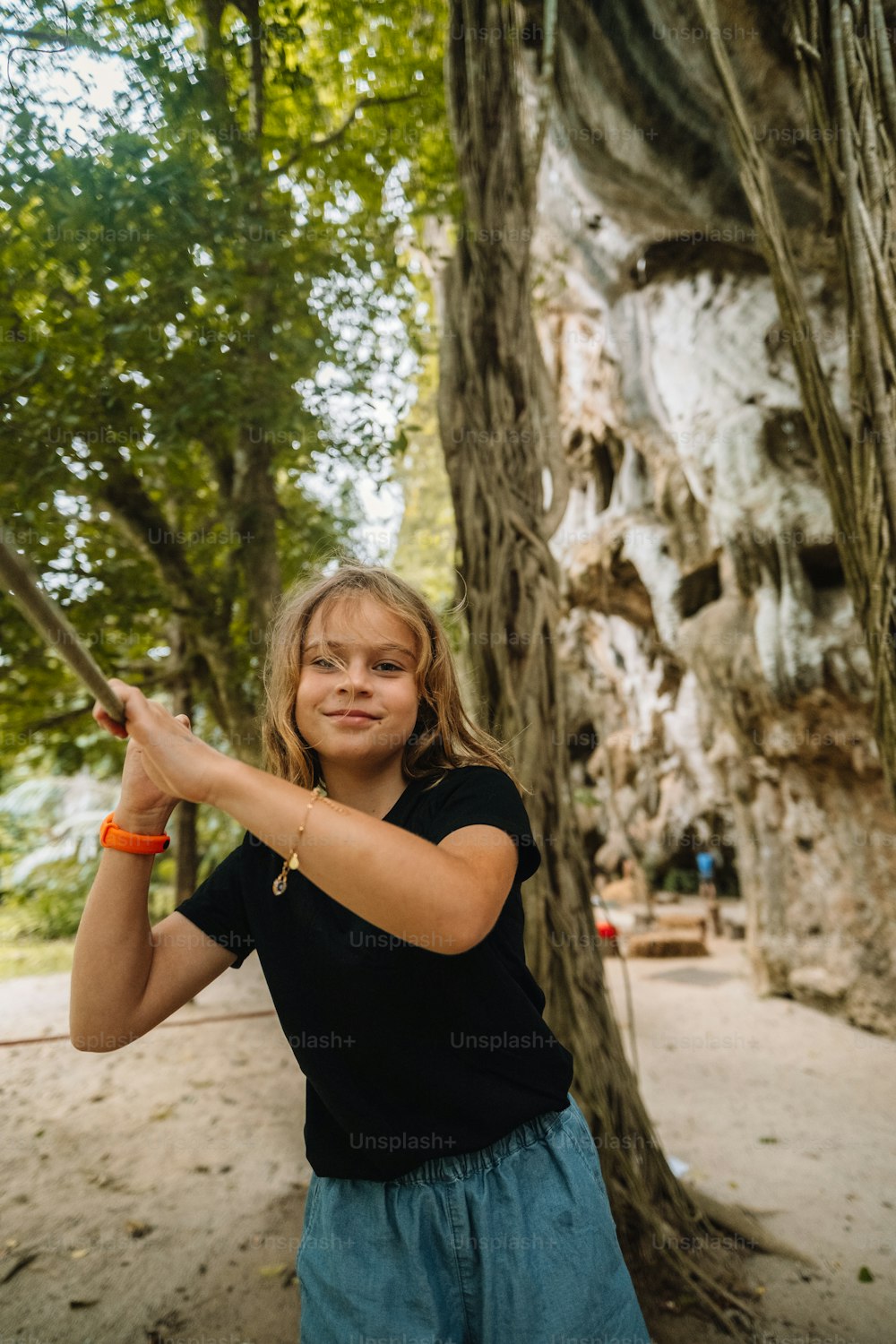 uma jovem segurando um taco de beisebol na frente de uma árvore