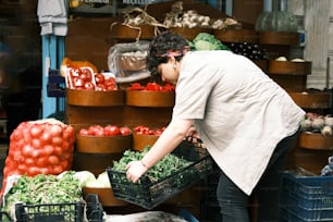 a woman is picking up vegetables at a market