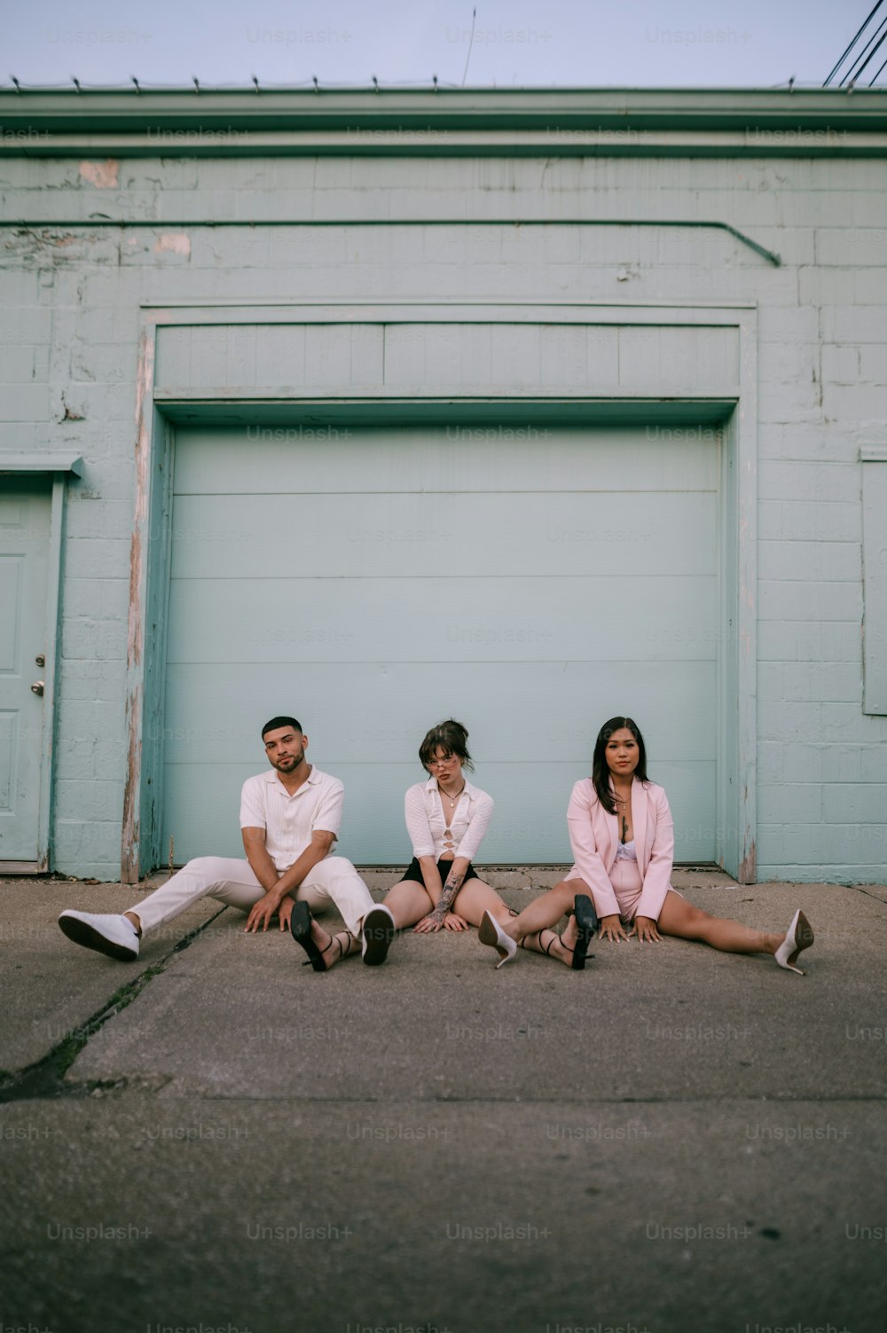 three people sitting on the ground in front of a garage door