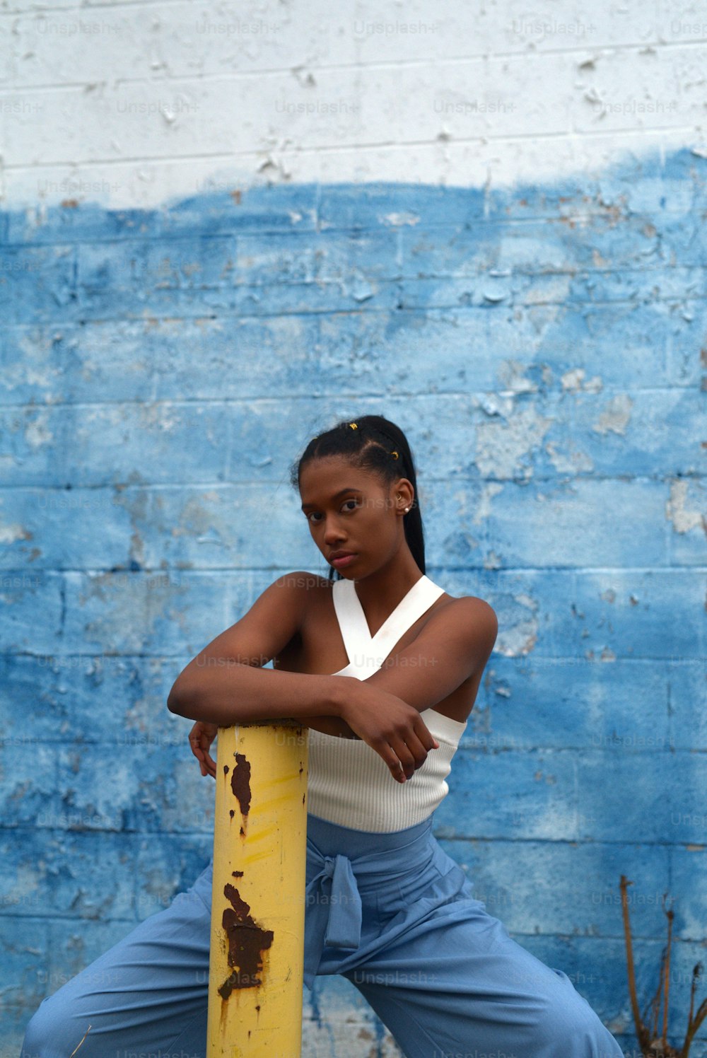 a woman leaning on a yellow pole in front of a blue wall